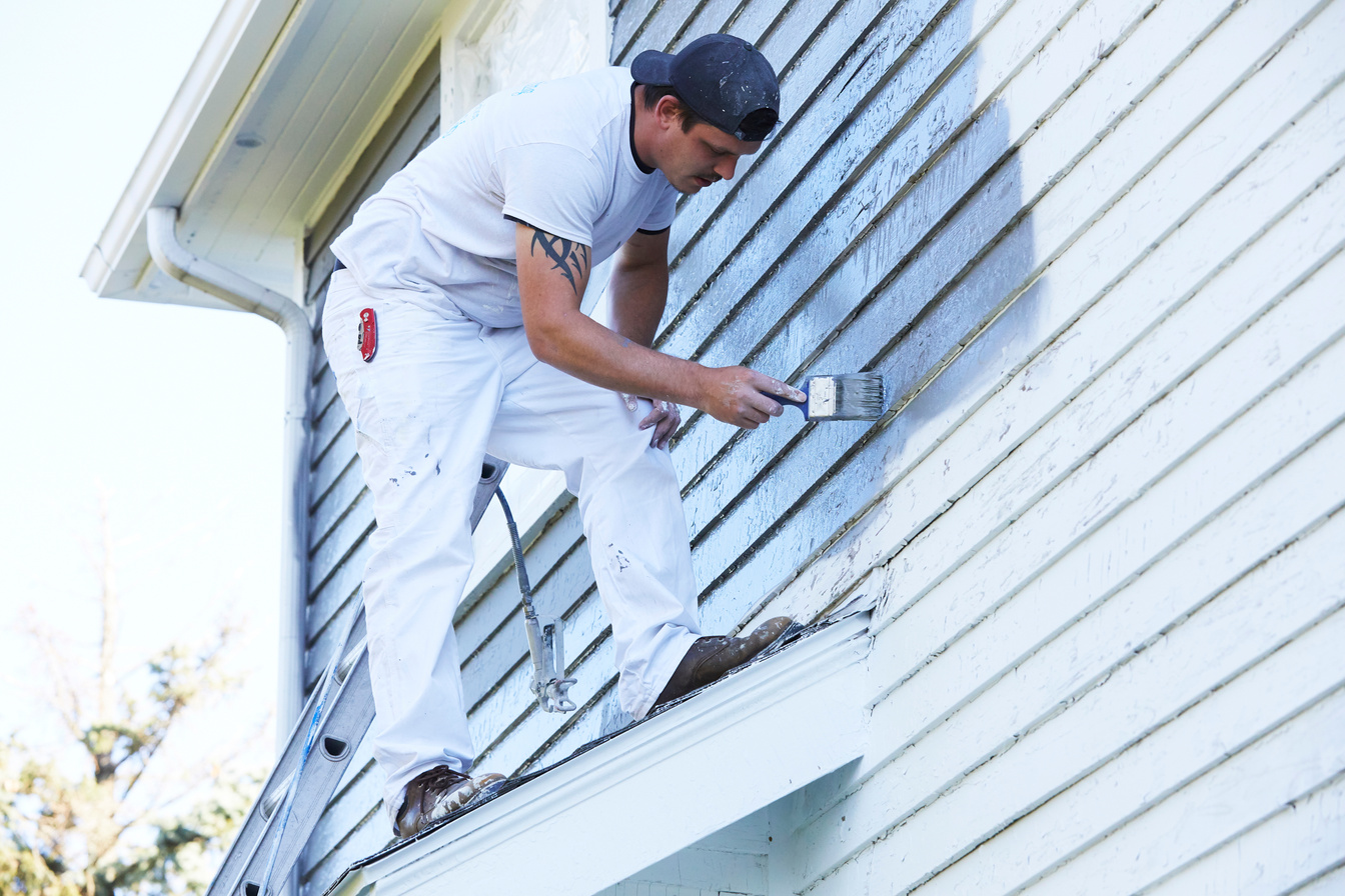 Man Brushing Paint On Exterior of Old Home
